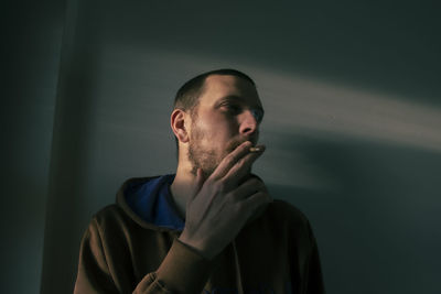 Portrait of young man looking away while standing against wall