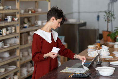 Side view of young woman using mobile phone while standing in kitchen