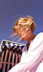 Low angle view of beautiful woman by hooded beach chair against clear blue sky