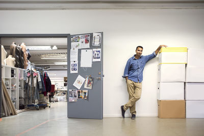 Full length of man standing by cardboard boxes at entrance of workshop