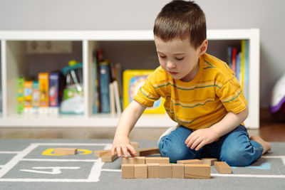 Little cute toddler boy three years playing wooden blocks in a home children's room