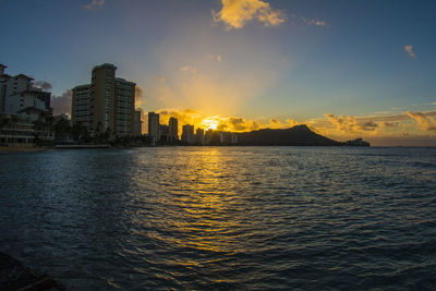 Scenic view of sea by buildings against sky at sunset