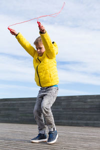 Full length of boy standing on yellow umbrella against sky