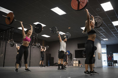 Athletes lifting barbell while exercising in gym