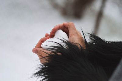 Cropped hands of woman holding heart shape snow on field
