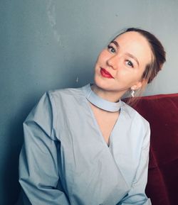 Portrait of young woman sitting against wall at home