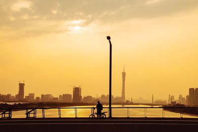 Silhouette man on promenade by river in city against sky during sunset