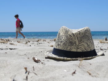 Sun hat on shore with woman in background at beach against sky