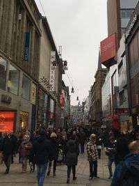 People walking on street amidst buildings in city against sky