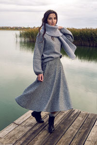 Woman stands next to the lake in a sweater and a scarf in the fall