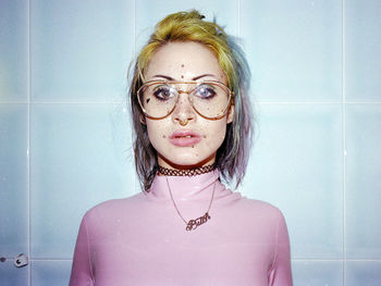 Portrait of young woman with freckles and pierced against tiled wall at bathroom