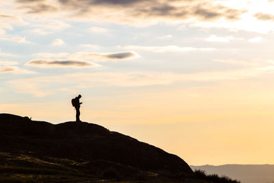 Silhouette man standing on rock against sky during sunset