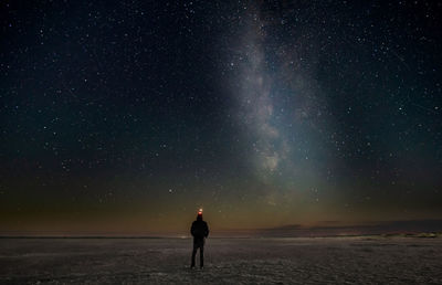 Rear view of woman standing on field against sky at night