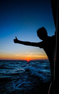 Silhouette man gesturing thumbs up while traveling in boat on sea during sunset