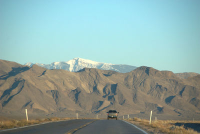 Road leading towards mountains against clear sky