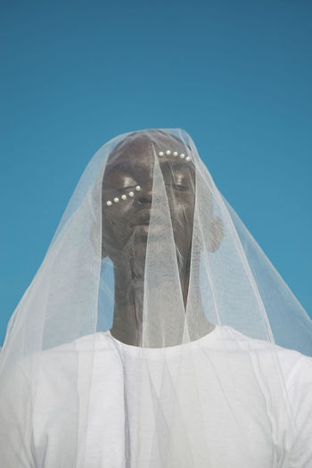 LOW ANGLE VIEW OF MAN COVERING FACE AGAINST BLUE SKY