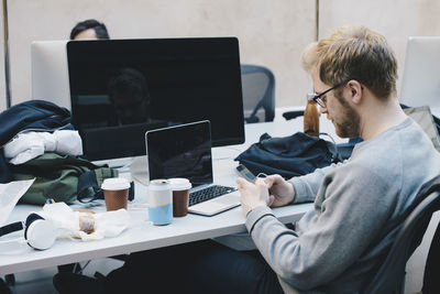 Side view of computer programmer using smart phone at desk in office