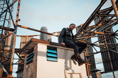 Low angle view of man sitting on staircase against sky