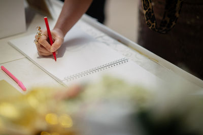 Cropped hand of woman writing in book on table