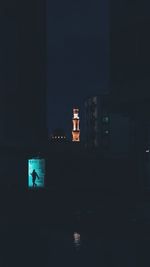 Silhouette person by illuminated building against sky at night