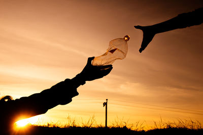 Silhouette hand holding orange sky during sunset