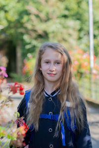 Back to school, portrait of a little girl from primary school outdoors, enjoying flowers 