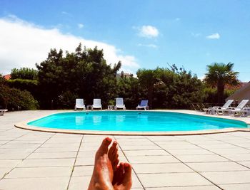 Low section of person by swimming pool against sky