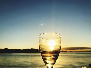 Close-up of wineglass against sea during sunset