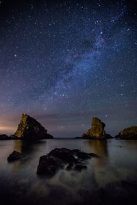 Rock formations in sea against star field at night