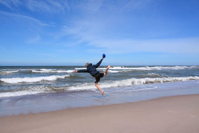 Rear view of playful man jumping on shore at beach