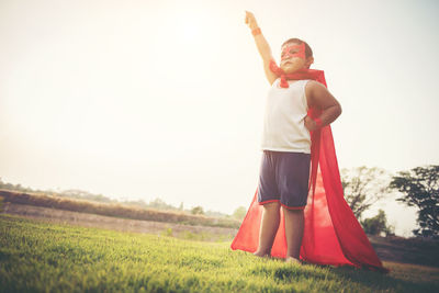 Low angle view of boy wearing cape and eye patch standing on grassy field against sky