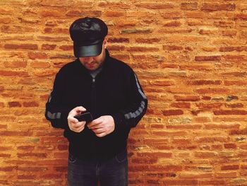 Man using mobile phone while standing against brick wall