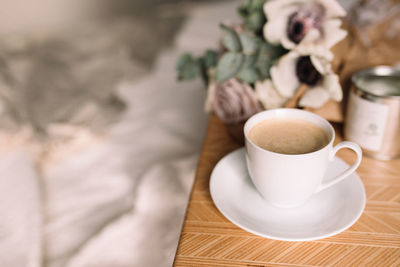 Romantic morning. wooden coffee table with flowers on bed with plaid, coffee cup, flowers and candle