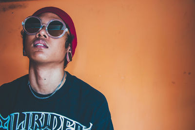 Portrait of young man wearing sunglasses standing against wall