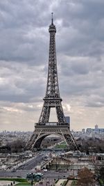 Communications tower in city against cloudy sky