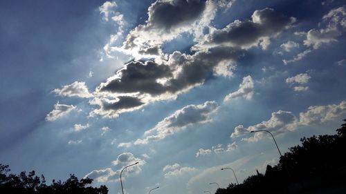 Low angle view of trees against cloudy sky