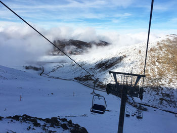 Ski lift over snowcapped mountains against sky