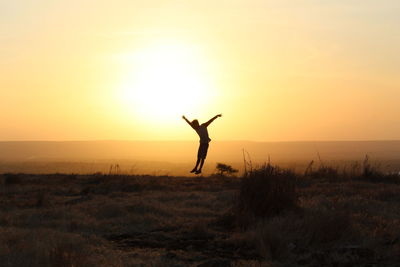 Silhouette person standing on field against sky during sunset