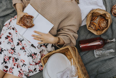 Mid section of woman lying on blanket with book and cinnamon bun