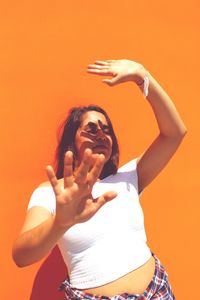 Young woman showing stop gesture while standing by orange wall
