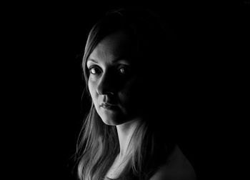 Close-up portrait of young woman against black background