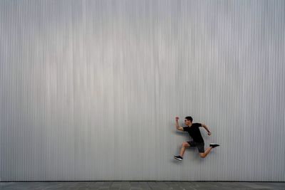 Side view of young man running against wall