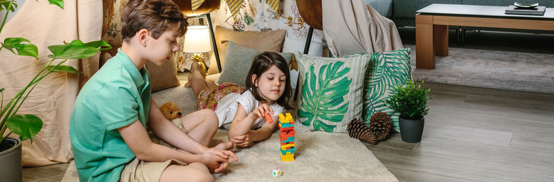 Banner of little girl catching wooden piece of stacking game while play with her brother living room