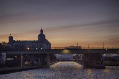 Bridge over river amidst buildings in city at sunset