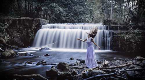 Young woman standing by waterfall in forest