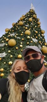 Portrait of couple wearing mask standing against christmas tree