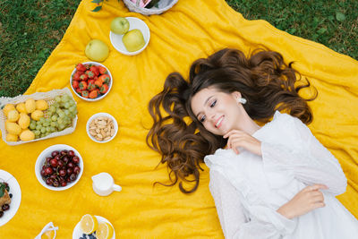 Top view of a beautiful romantic woman in a dress, lying on the green grass on a yellow blanket