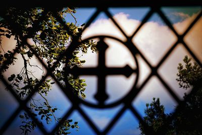 Close-up of cross on metal grate against sky