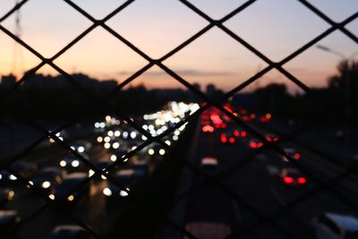 Defocused image of illuminated chainlink fence against sky during sunset