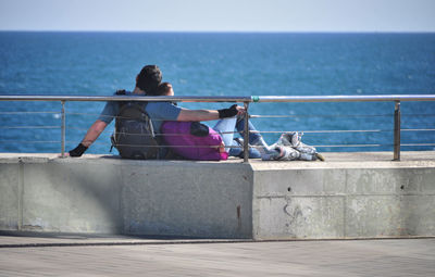 Rear view of women sitting on railing against sea